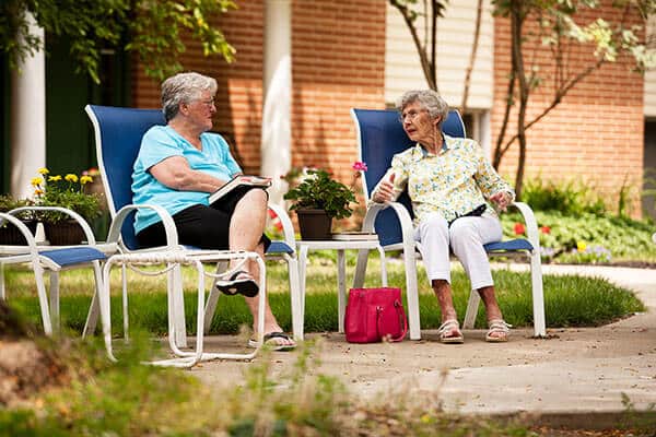 Two elderly women sitting outside in chairs conversing.