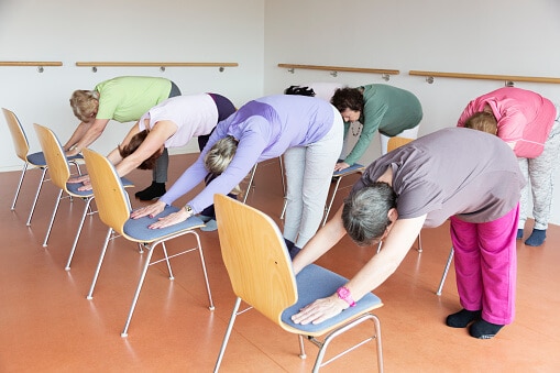 senior women exercising yoga and pilates using chairs, doing the downward facing dog position,