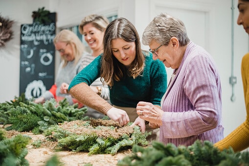 Senior woman is getting assistance from the florist at her Christmas wreath-making workshop.