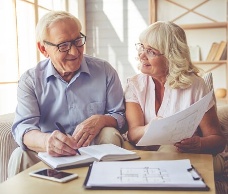 Senior man and woman, a couple, are discussing house project, making notes and smiling while sitting on couch at home