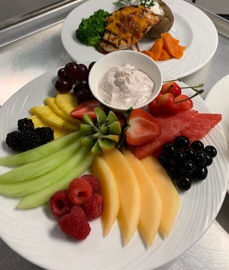 dinner plate of sliced fruit, dipping sauce, plate of chicken and potatoe