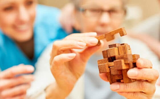 therapist helping elderly woman with a jenga style memory care activity