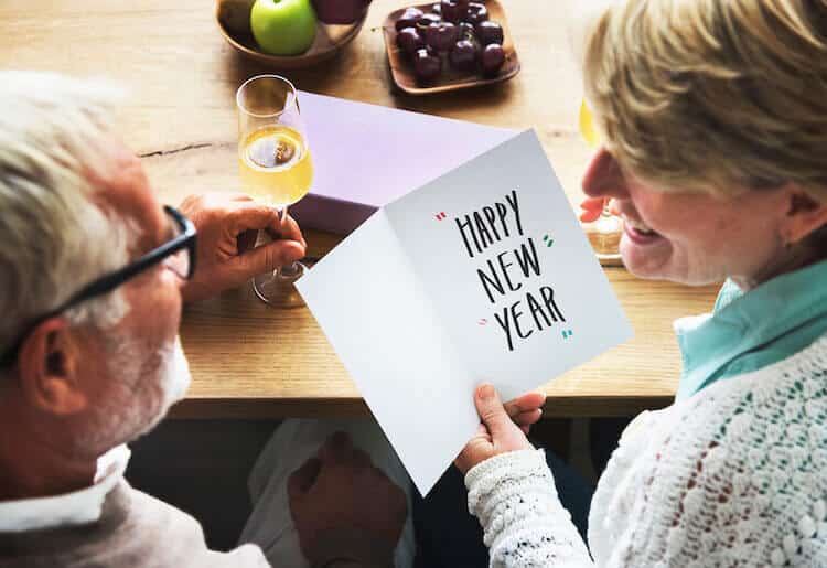 A couple, a senior man and senior woman, look at a card that reads Happy New Year