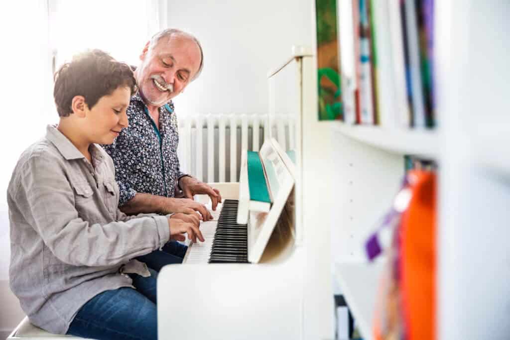 A senior man and his grandson playing the piano together on a white piano