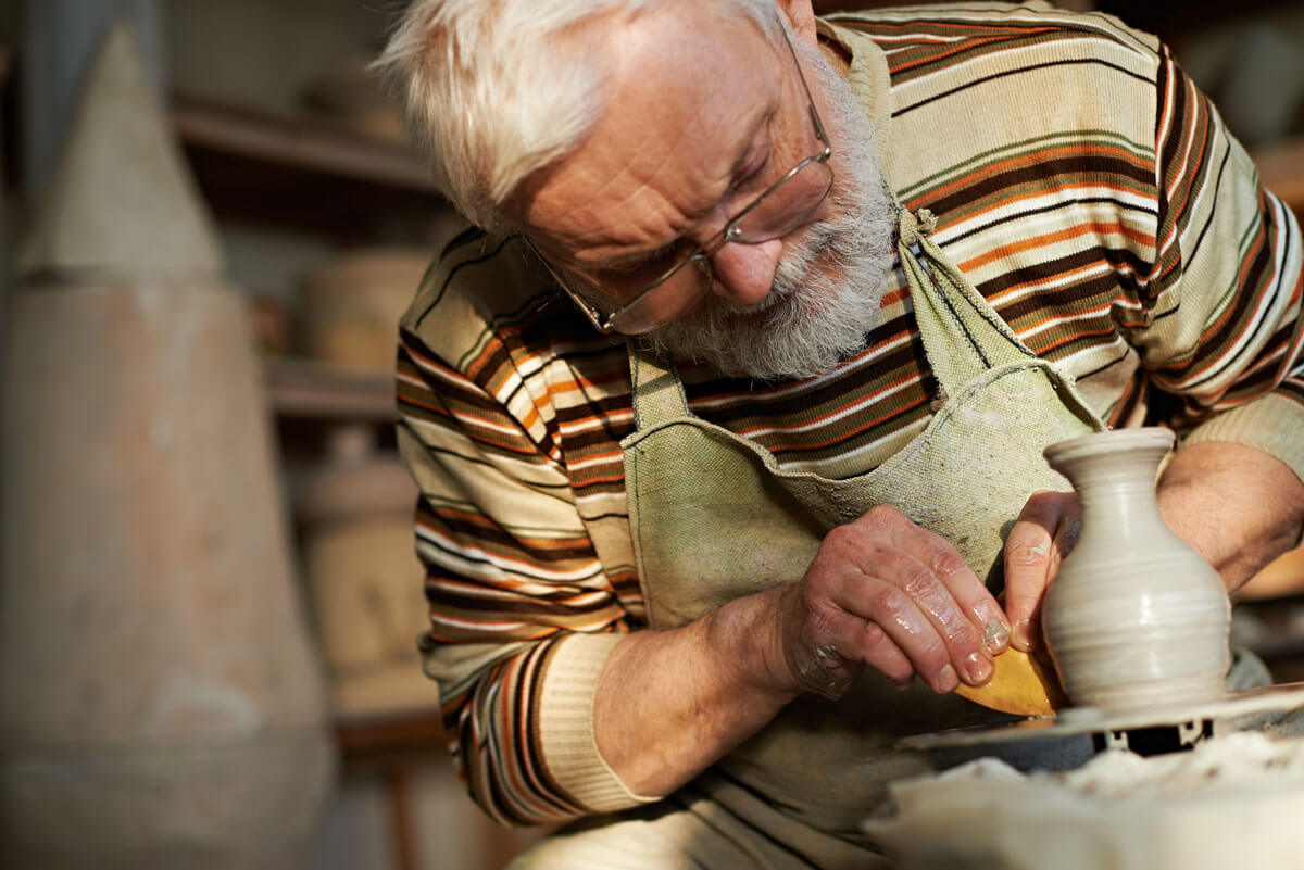 A senior man works on crafting a vase from clay on a potter's wheel