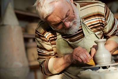 A senior man works on crafting a vase from clay on a potter's wheel