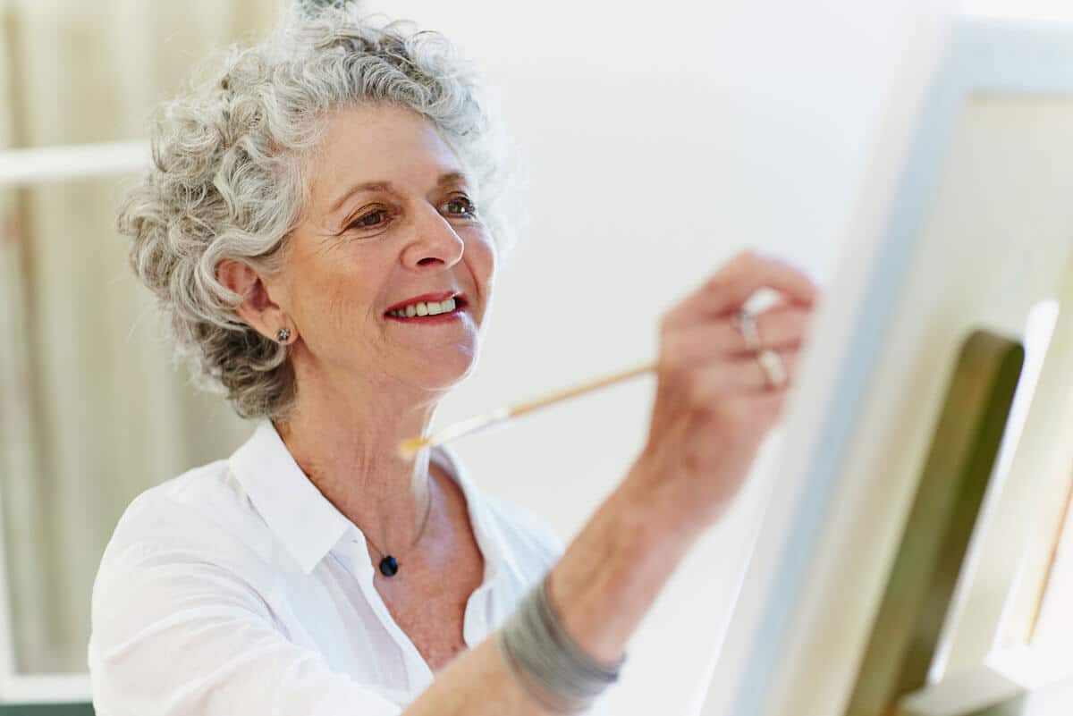 A senior woman smiling and painting on a canvas