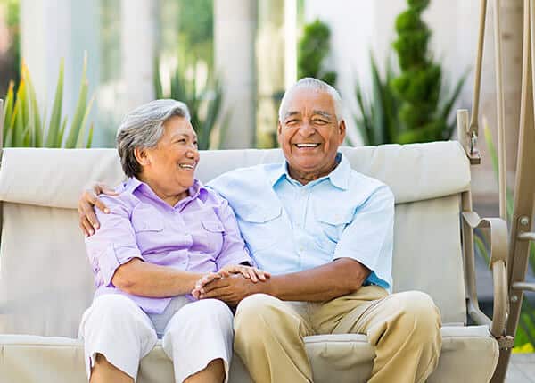 An older couple sitting together on a couch smiling and holding each other.