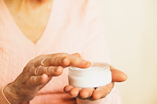 elderly woman applies lotion to her palm