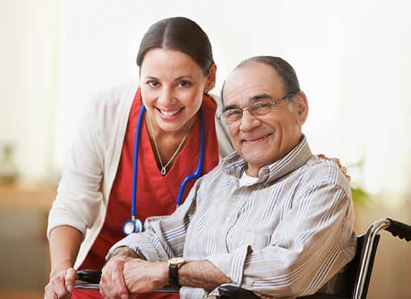 A nurse with an elderly man in a wheel chair smiling at the camera.