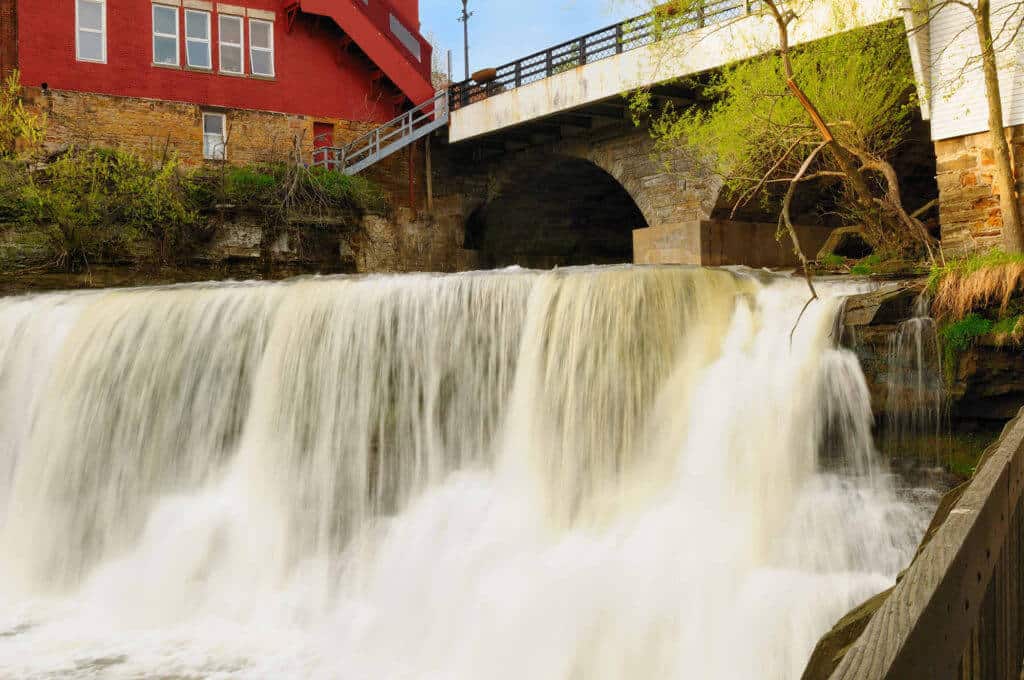 Photo of the Chagrin Waterfall in summer. You can see a stonework bridge and a historic home painted red next to the falls.