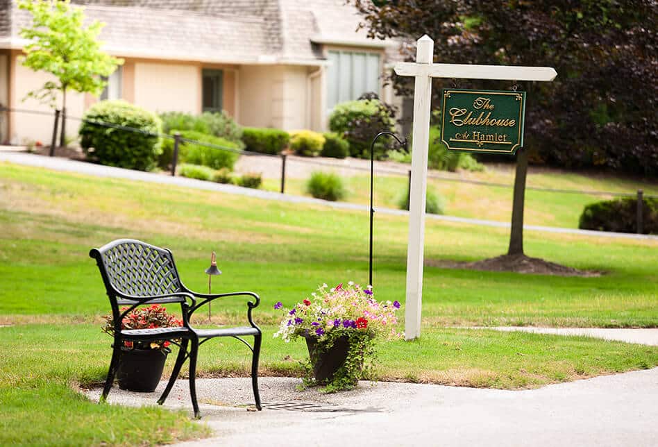 A bench and flowers near the sign for the Hamlet Clubhouse.