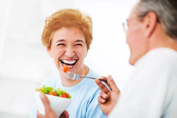 A senior couple laugh and smile while eating a fresh salad